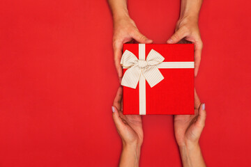 Man giving red gift box with gold ribbon to woman on red background. Top view. Gift for birthday, Valentine's Day, Christmas or New Year