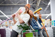 happy man and woman enjoy shopping, have fun, sing and dance holding mops, man with bucket on head, they laugh