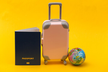 International travel concept. Mini pink plastic travel suitcase with globe, passport on yellow background. Minimal style