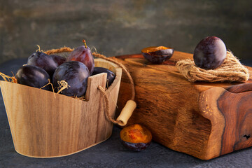 Poster - Still life of plums in a wooden basket with hay and a wooden stand on a purple background