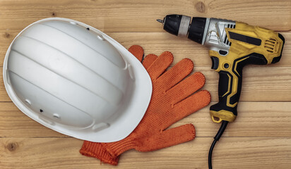 Wall Mural - Old drill screwdriver and protective helmet, gloves on a wooden background. Top view