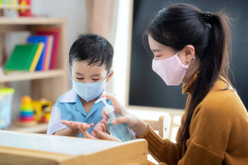 asian woman teacher use alcohol gel on hand of her student for prevent virus from covid19 in classro