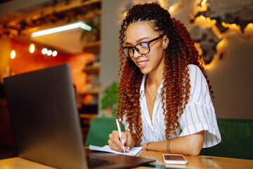 Young freelancer woman using laptop computer sitting at cafe table. Smiling woman working online or studying and learning while using notebook. Business People Concept