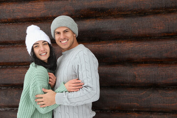 Canvas Print - Lovely couple wearing warm sweaters and hats near wooden wall. Winter season