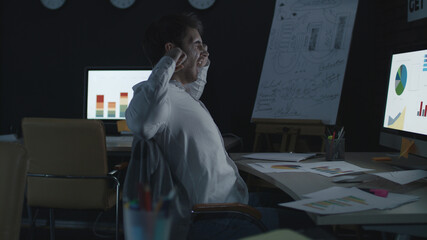 Tired businessman stretching and yawning near computer in night office