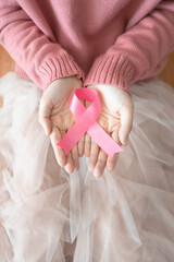 Wall Mural - International symbol of Breast Cancer Awareness Month in October. Closeup of female hand holding satin pink ribbon awareness on her knee. Women's health care and medical concept. Copy space. Vertical.