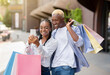 © Prostock-studio - Bonuses, gifts and cashback after shopping. Happy couple with many color bags looks at smartphone