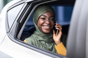 Wall Mural - Black muslim woman traveling on car back seat and talking on cellphone