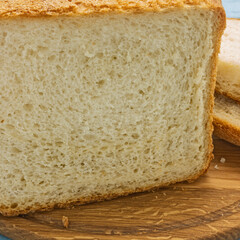 Freshly baked white bread close-up. Golden crust, porous flesh. There are crumbs on a wooden cutting board. Homemade baking.