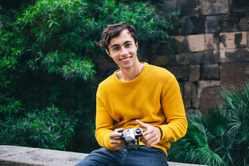 Portrait of cheerful young male in trendy wear visiting town on holiday trip making pictures of locations,smiling hipster guy looking at camera taking photos on leisure and hobby outdoors on sunny day