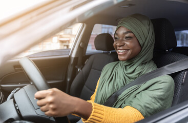 Wall Mural - Happy Black Muslim Woman In Hijab Driving Car With Fasten Seat Belt