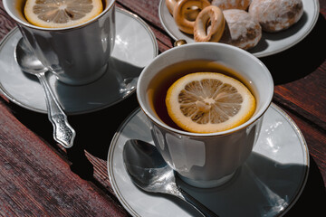 A shiny little teaspoon for tea with sugar. Black tea with lemon and sweets in a beautiful white bowl stands on a wooden table.