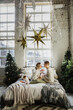 © Oksana - Young women and a man hold a newborn in their arms in the room near the Christmas tree. Family with a newborn and a dog on the bed in a Christmas interior.