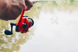 Close up of spinning with the fishing reel in the hand, fishing hook on the line with the bait in the left hand against the background of the water.