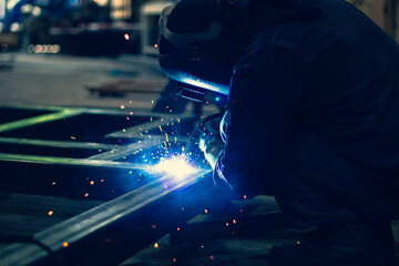 welder Industrial automotive part in factory. Workers wearing industrial uniforms and welding masks at a welding factory protect from welding sparks. Occupational safety concept