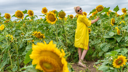 Joyful woman in a yellow dress, young with a charismatic appearance on the background of a field with sunflowers in hot sunny weather