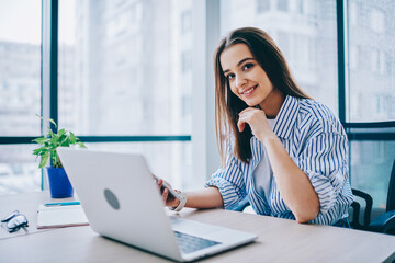 Wall Mural - portrait of happy female trainee in smart casual wear sitting at office desktop and smiling at camer