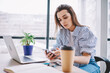 © BullRun - Caucasian female freelancer checking mobile notification during remote job in modern workspace, skilled millennial in smart casual wear making online booking and banking via smartphone application