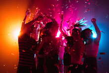 Confetti. A Crowd Of People In Silhouette Raises Their Hands, Dancing On Dancefloor On Neon Light Background. Night Life, Club, Music, Dance, Motion, Youth. Bright Colors And Moving Girls And Boys.