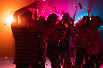 Festive. A crowd of people in silhouette raises their hands, dancing on dancefloor on neon light background. Night life, club, music, dance, motion, youth. Bright colors and moving girls and boys.