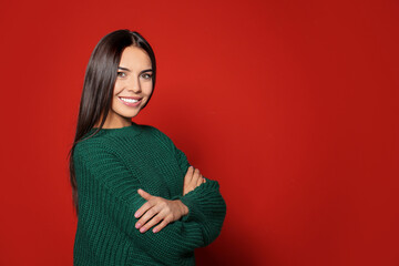 Wall Mural - Happy young woman wearing warm sweater on red background. Space for text