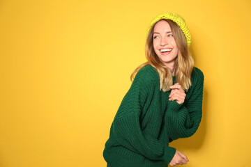 Poster - Happy young woman wearing warm sweater and knitted hat on yellow background. Space for text