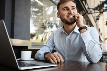 Wall Mural - Happy young man with laptop talking on phone at outdoor cafe