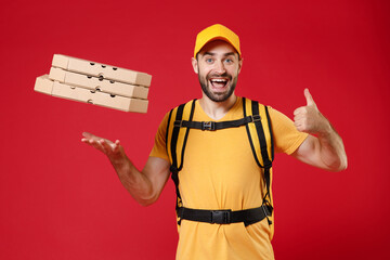 Wall Mural - Fun delivery man in yellow cap t-shirt thermal bag backpack with food throw toss up pizza in cardboard flatbox showing thumb up isolated on red background studio Guy male employee work courier service