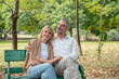 © Sathaporn - Happy Senior Caucasian couple hugging and holding hand together in while sitting at bench in the park.