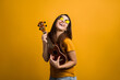 Attractive girl with long hair having fun with ukulele and modern glasses.