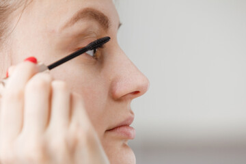 A young girl paints her eyelashes with mascara. Face close-up. facial care