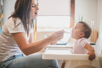 Mother feed her little daughter with a spoon