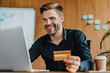 © InsideCreativeHouse - Young man holding credit card and doing online banking on laptop in office