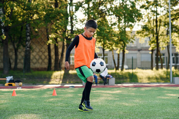 Motivated hispanic teen football player stuffs soccer ball on leg. Practicing sport exercises at artificial stadium.