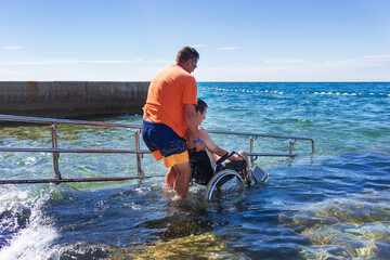 Wall Mural - Accessible beach with ramp for disabled people. Man on wheelchair going swimming.