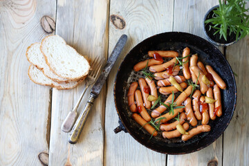 Wall Mural - Appetizing juicy mini sausages in a frying pan on the table. Rustic style. Flat lay.