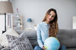 © BestForYou - Smiling woman holding globe sitting on the couch at home. Travel planning.