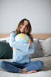 © BestForYou - Cheerful young woman hugging globe sitting on the couch at home.