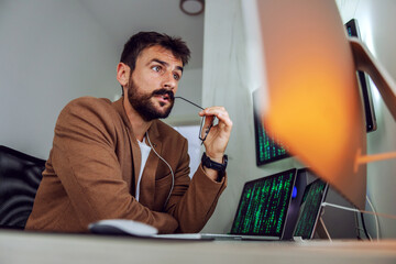 Young attractive bearded programmer dressed business casual sitting in his office and working on important project.