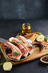 Poster - Raw lamb ribs with ingredients for cooking: salt, pepper, olive oil and herbs on a plate with a wooden handle