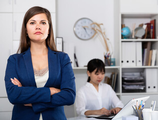 Wall Mural - Portrait of young positive business woman standing in office, colleague working on background