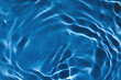 Blurred transparent dark blue colored clear calm water surface texture with splashes and bubbles. Trendy abstract nature background. Water waves in sunlight with copy space.