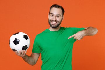 Wall Mural - Funny young man football fan point index finger on green t-shirt cheer up support favorite team with soccer ball isolated on orange background studio portrait. People sport leisure lifestyle concept.