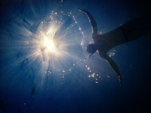 Man Silhouette Underwater With The Sun Shining In Background Through The Sea. Filtered Image, Low Key Post Production.
