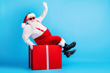 Full Length Photo Of Fat Overweight Santa Claus With Big Stomach Beard Sit Red Gift Box Greeting X-mas Christmas Party Wear Suspenders Overalls Sunglass Isolated Blue Color Background