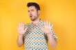 © Roquillo - Young man wearing hawaiian shirt over yellow isolated background Moving away hands palms showing refusal and denial with afraid and disgusting expression. Stop and forbidden.