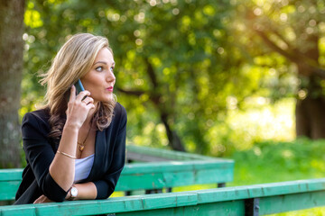 Wall Mural - a young emotional blonde woman in the park talking on the phone