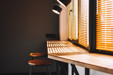 Modern wooden table on the kitchen near big window with curtain. Warm light. Interior detail.