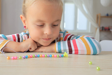 Little girl is making bracelet from beads