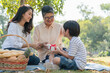 © Supachai - Happy Asian family a boy giving gift box to grandmother while picnicking in the park